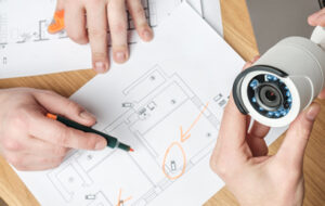 Security professionals reviewing a floor plan and surveillance camera while planning camera placement.