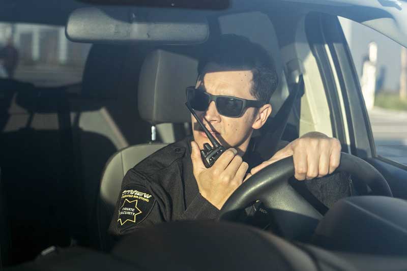 OnView security officer driving a patrol vehicle and communicating by radio with a monitoring agent.